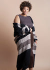 Smiling woman with curly hair wears a sleeveless brown dress and a long, striped cardigan. Neutral background, conveying warmth and comfort.