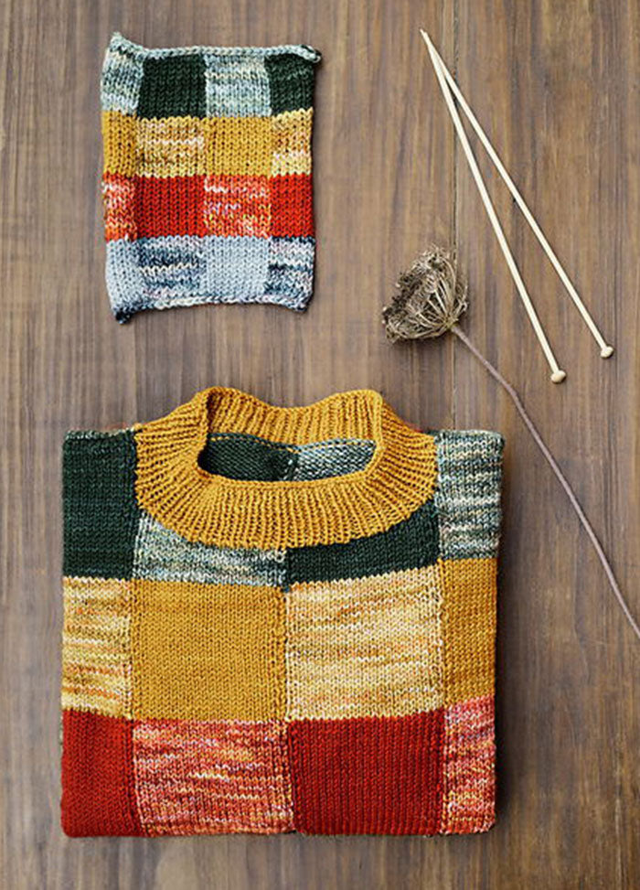 Berta Sweater with patchwork squares in green, yellow, red, and gray, shown with a matching swatch, knitting needles, and yarn.