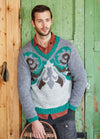 A man with a thoughtful expression leans against a rustic green door. He wears a colorful sweater with teal and brown patterns over a rust shirt.