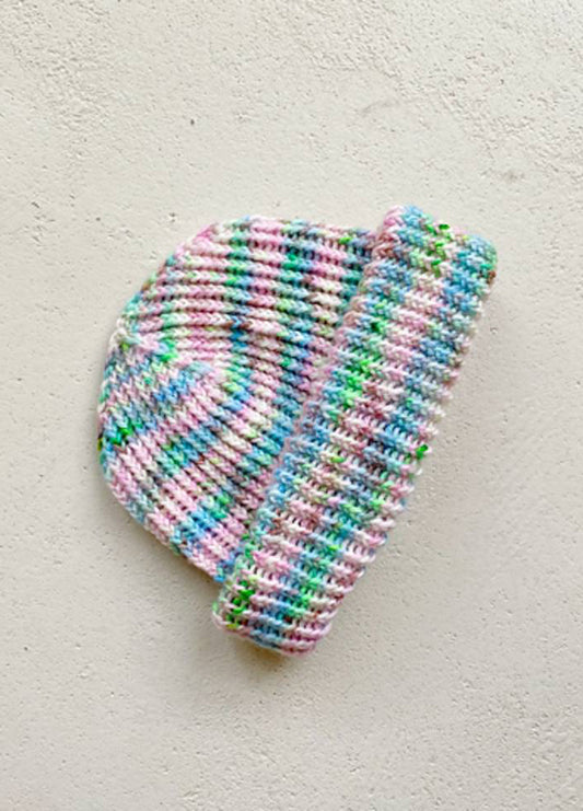 Multicoloured knitted hat with pastel stripes of pink, blue, green, and white, laid flat against a textured light grey background. Cozy and vibrant.