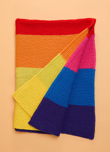 Folded hand-knitted Brighton Blanket featuring horizontal stripes in vibrant rainbow colors – red, orange, yellow, green, blue, and purple – showcasing bold and cheerful design.