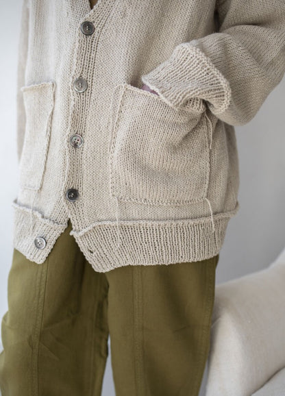 Close-up of a person wearing a beige knit cardigan with buttons and two pockets, paired with olive green pants. The mood is relaxed and casual.