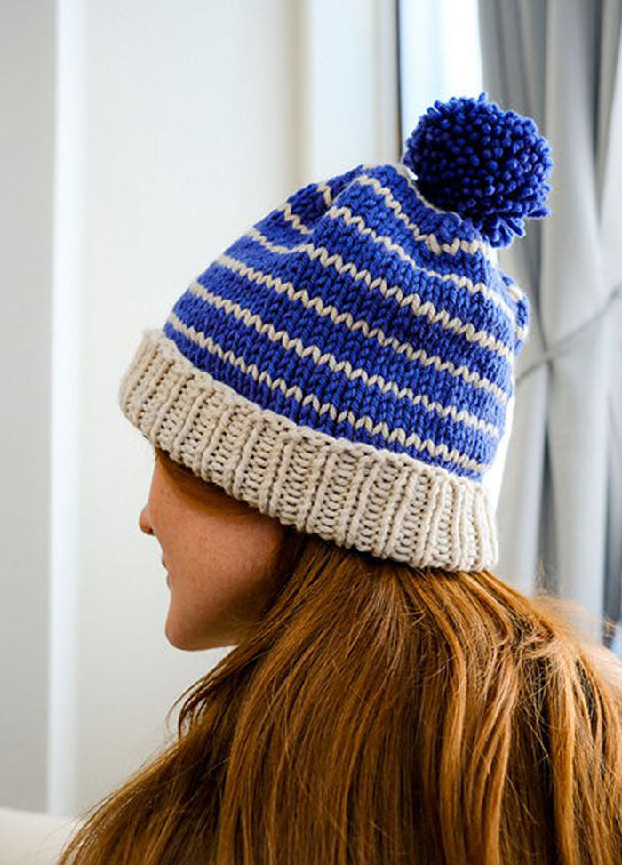 Blue and white striped Cardo Holiday Hat with a blue pom-pom and beige ribbed brim, shown from the back on a model.