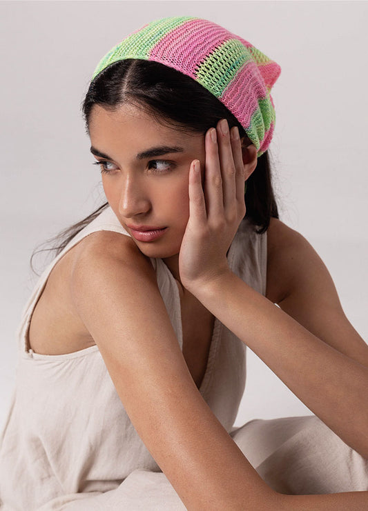 Person wearing the Chalcito Scarf with horizontal pink and green stripes, dressed in a sleeveless light-colored top, resting hand on face.
