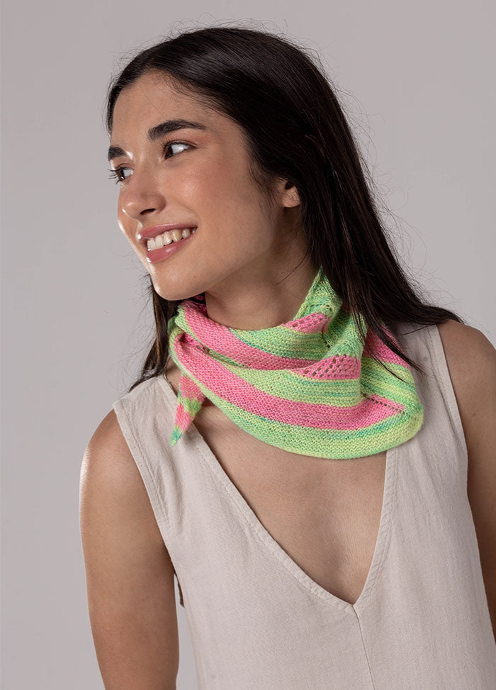 Person wearing Chalcito Scarf with alternating pink and green stripes, wrapped around neck over sleeveless beige top.