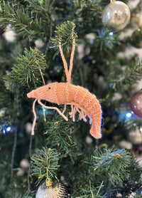 Knitted prawn Christmas ornament hanging on a decorated tree with baubles and lights.