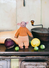 Alphonse & Mira the Pigs: knitted pig in orange sweater and checkered pants, posed among vegetables on a kitchen counter.