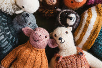 Characters: group of intricately knitted stuffed animals including a pig in an orange sweater and a bear in brown overalls.