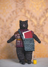 Giorgio the Cat: black knitted cat in a multicolored sweater with a blue bag holding a red book, beside a bottle of yellow pencils.