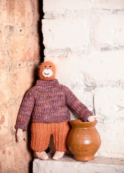 Henri the Orangutan: knitted orangutan in a purple sweater and orange pants, posed beside a small clay pot.