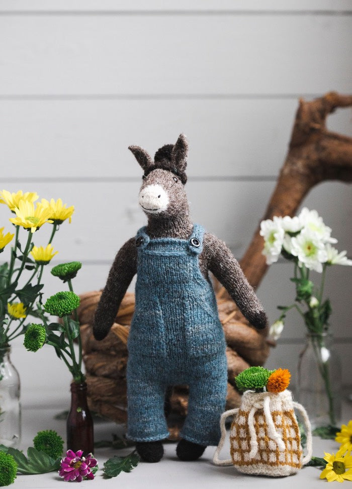 Horacio the Donkey: knitted donkey in blue overalls, surrounded by flowers and a bag with an orange pom-pom.