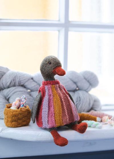 Nanna the Lady Duck: knitted duck in a striped dress, seated near yarn skeins and a basket of colorful yarn balls.