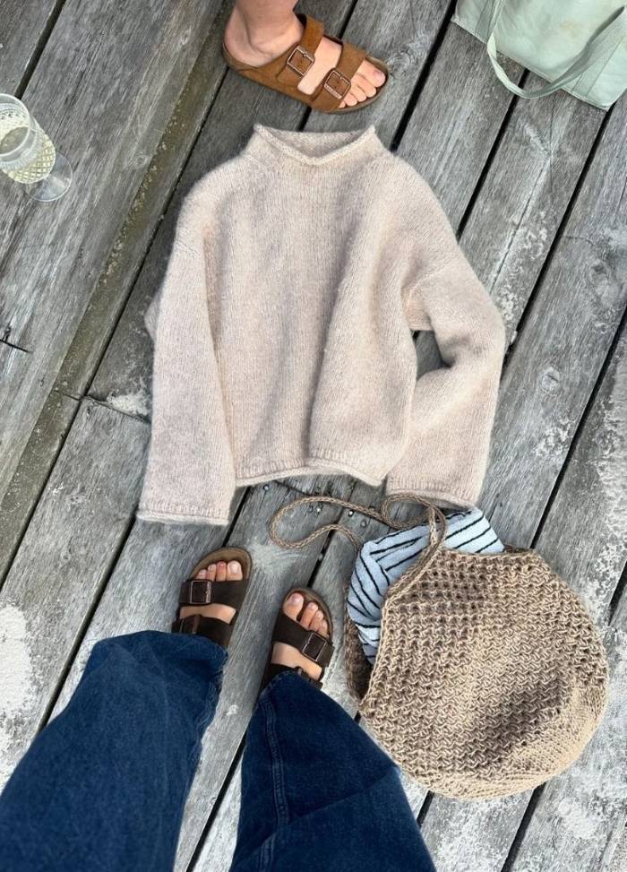Brown sandals on deck, alongside a beige sweater, a striped shirt, and a woven bag, convey a relaxed, casual outdoor vibe.