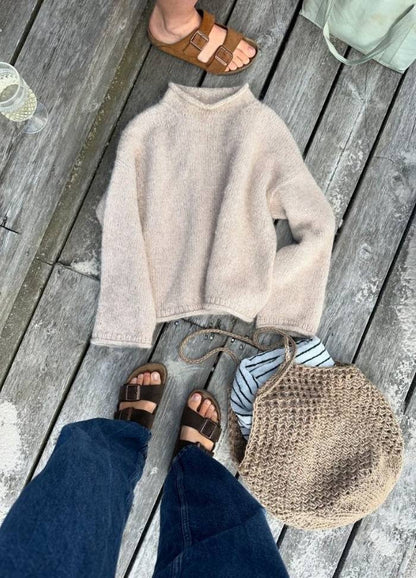 Brown sandals on deck, alongside a beige sweater, a striped shirt, and a woven bag, convey a relaxed, casual outdoor vibe.