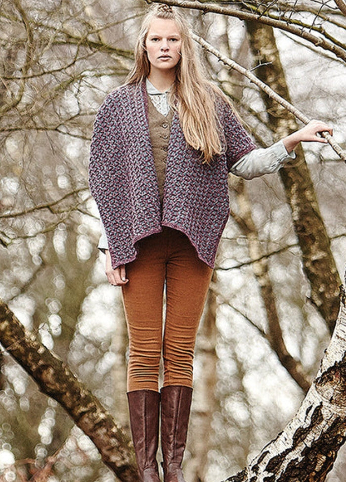 Person wearing the Connemara Jacket, a textured open-front knit design, styled with brown pants and boots in a wooded outdoor setting.