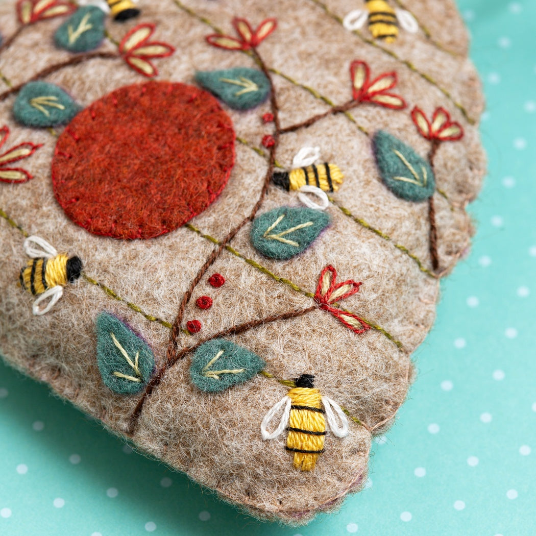 Embroidered fabric piece with bees, flowers, and leaves on a teal background