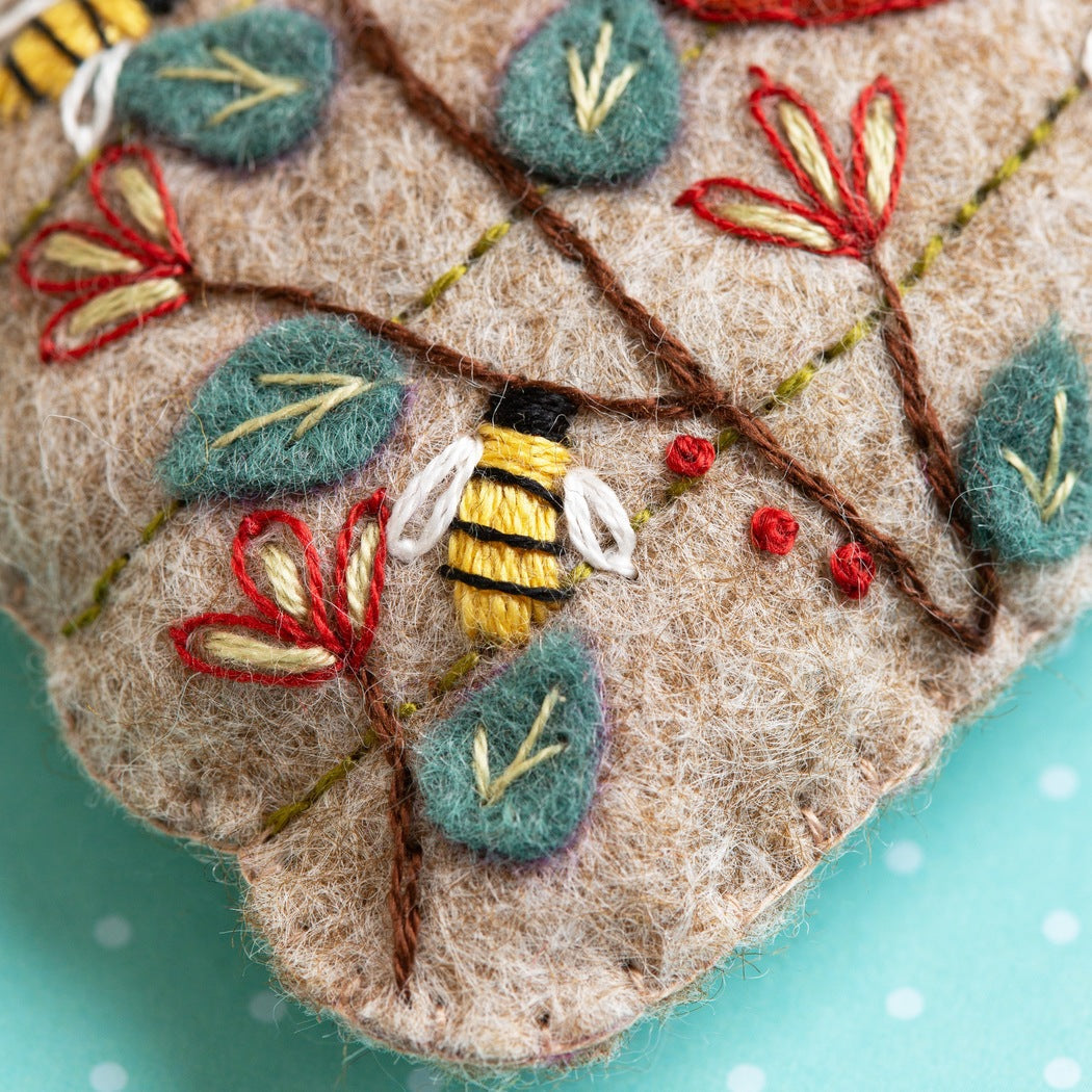Embroidered fabric piece with a bee and leaves on a teal background