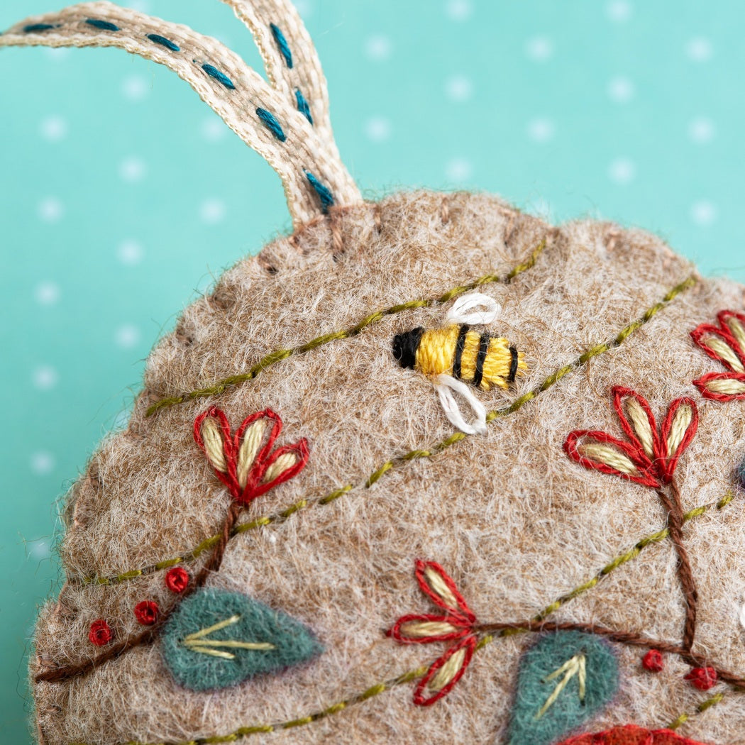 Embroidered leaf ornament with a bee and flowers on a teal background