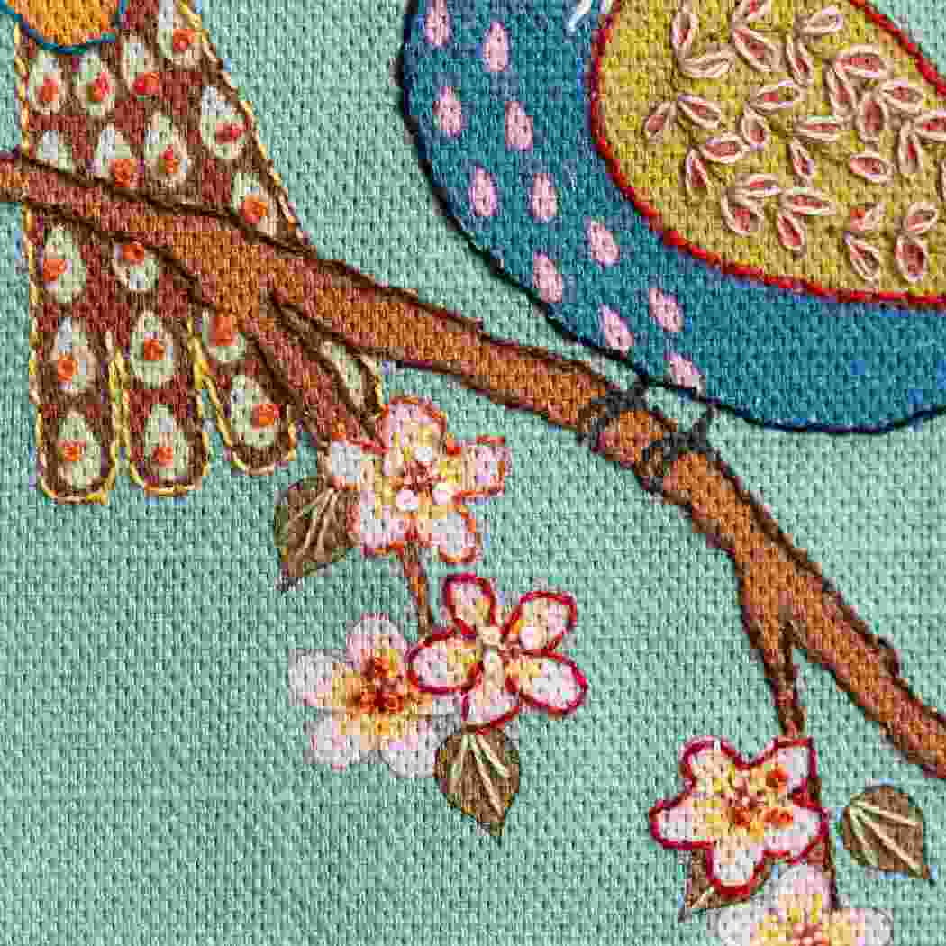 Colorful embroidered design of a branch with flowers and leaves on a light blue background