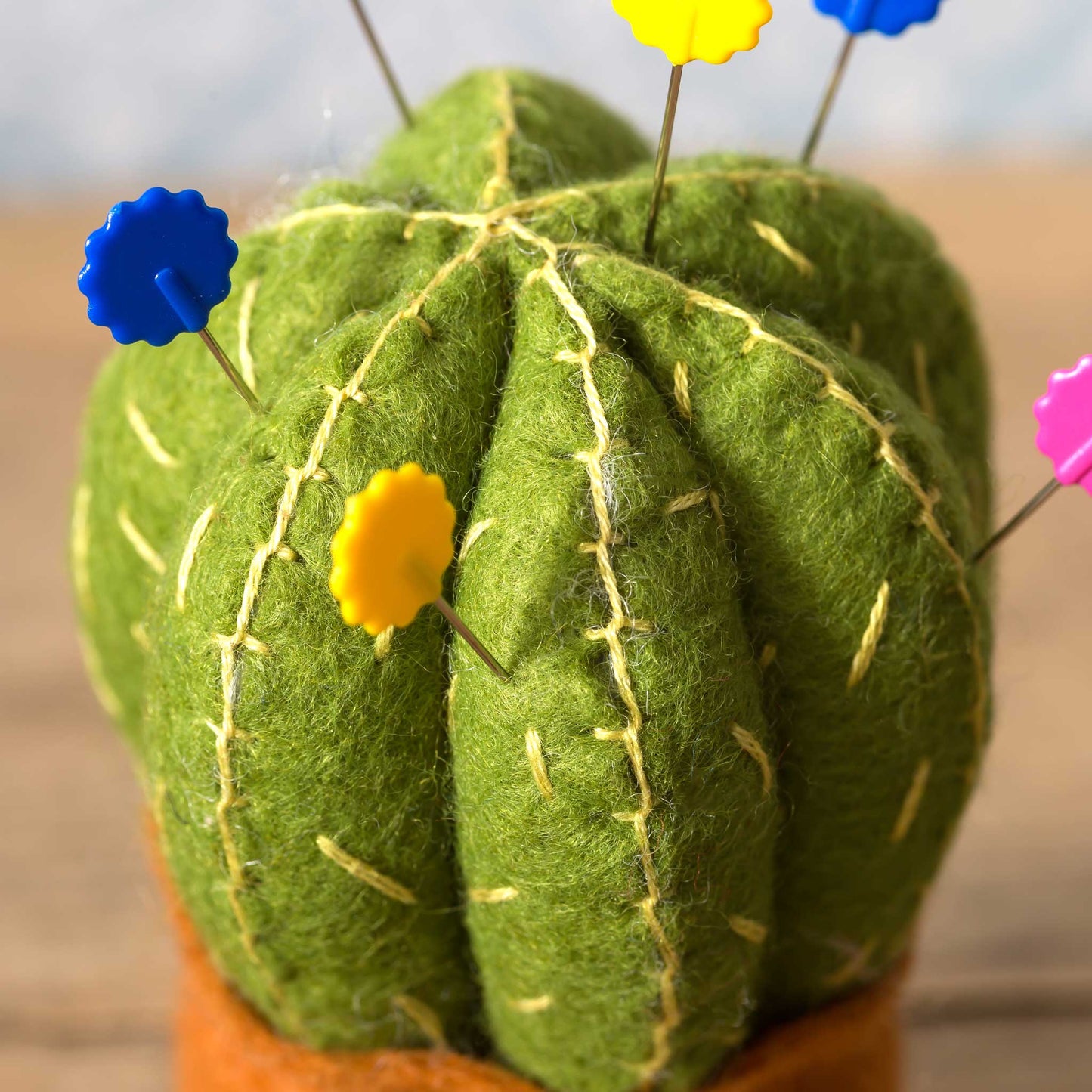 Green felt cactus with colorful pins on a blurred background
