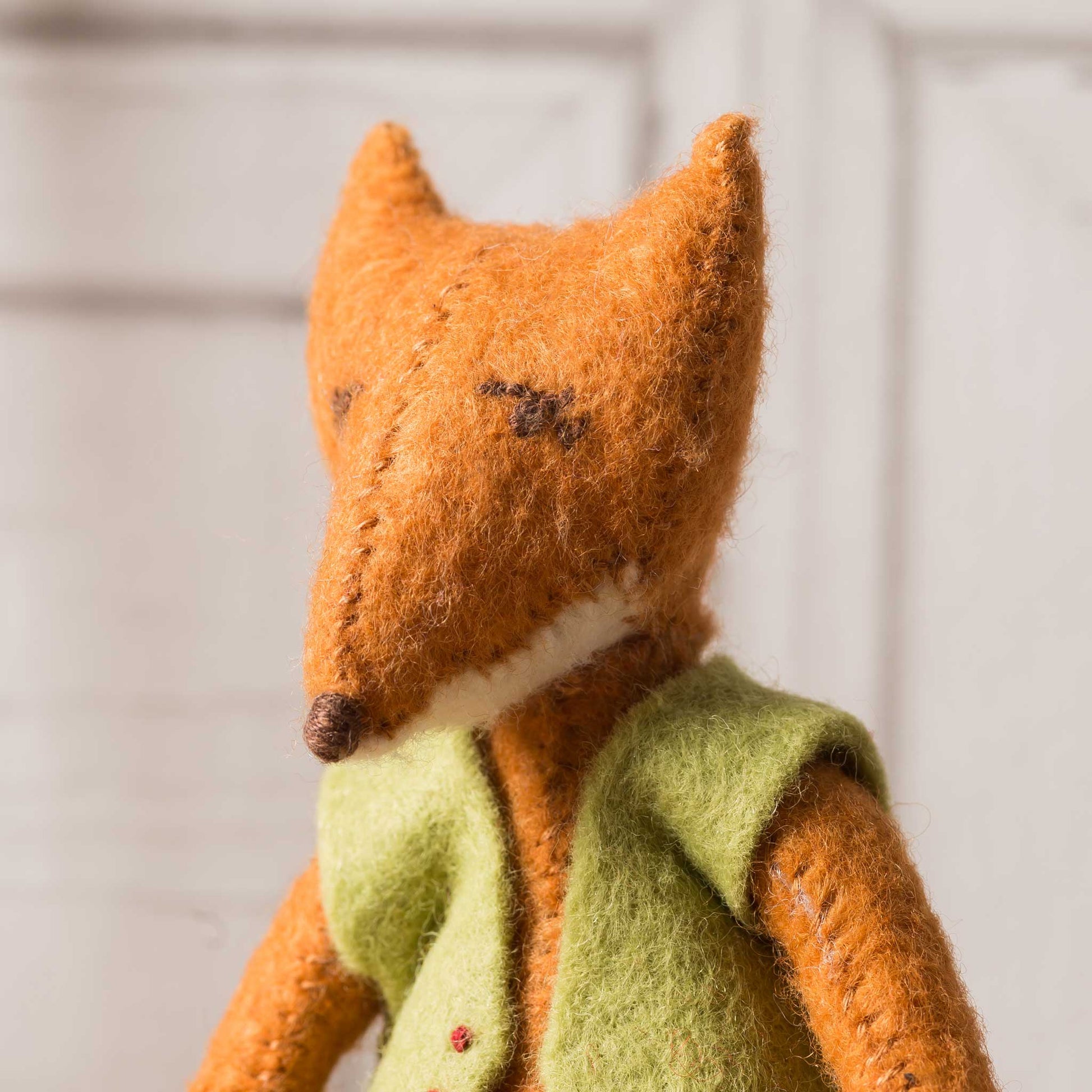 Stuffed fox toy wearing a green sweater against a neutral background