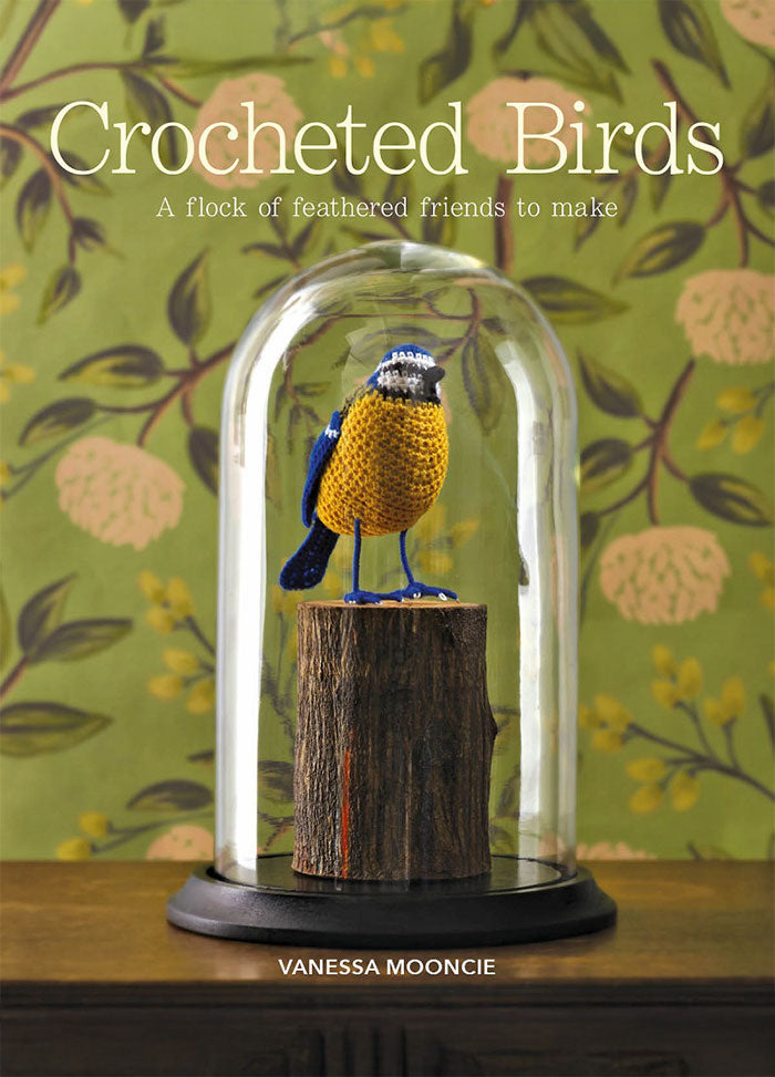 Cover of “Crocheted Birds” by Vanessa Mooncie, featuring a crocheted bird perched on wood inside a glass dome. The subtitle reads “A flock of feathered friends to make,” set against a green floral background.