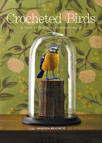 Cover of “Crocheted Birds” by Vanessa Mooncie, featuring a crocheted bird perched on wood inside a glass dome. The subtitle reads “A flock of feathered friends to make,” set against a green floral background.
