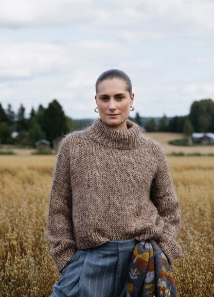 Albarn Sweater': Brown high-collared knitted sweater worn outdoors in a field with trees and buildings in the background.