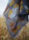 Butterfly Sampler Scarf': Grey knitted scarf with yellow and orange butterfly motifs, displayed over tall grass.