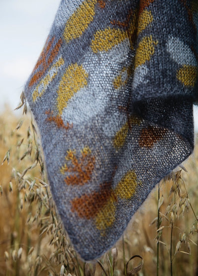 Butterfly Sampler Scarf': Grey knitted scarf with yellow and orange butterfly motifs, displayed over tall grass.
