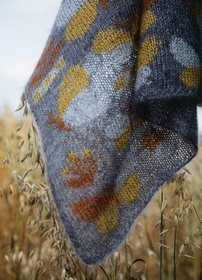 Butterfly Sampler Scarf': Grey knitted scarf with yellow and orange butterfly motifs, displayed over tall grass.