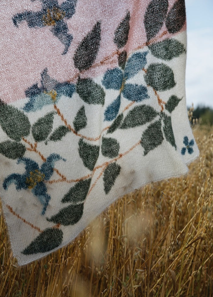 Clematis Scarf': Botanical scarf with green leaves and blue clematis flowers on a white-to-pink gradient background, displayed over tall grass.