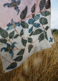 Clematis Scarf': Botanical scarf with green leaves and blue clematis flowers on a white-to-pink gradient background, displayed over tall grass.