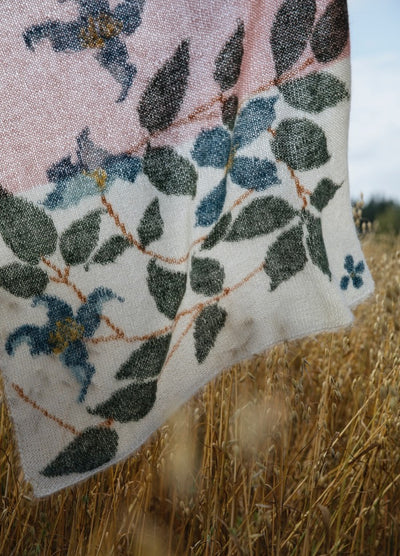 Clematis Scarf': Botanical scarf with green leaves and blue clematis flowers on a white-to-pink gradient background, displayed over tall grass.