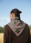 Embroidered Achillea Scarf': Light gray scarf with embroidered berries and leaves in red, pink, and purple, worn with a brown sweater.