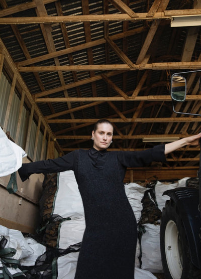 Frankie Dress': Black dress worn inside a wooden structure with high beams, surrounded by large white bags and a vehicle.