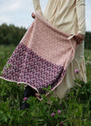 Garden Party Scarf': Two-toned scarf with light pink and dark purple floral patterns, held in a field of green plants and purple flowers.
