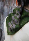 In The Wild Scarf': Green scarf with gray floral pattern, worn with twisted braid hairstyle and silver hoop earrings.