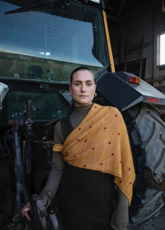 Peony Scarf': Yellow scarf with red square patterns, draped over shoulder in front of a large tractor indoors.