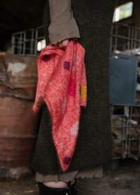 Pressings Scarf': Colorful scarf in red, pink, yellow, and white tones with patterns, held by person in green knitwear and beige pants.