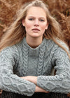 Person wearing the Dartmoor Sweater, a grey cable-knit design with detailed patterns on sleeves and front, photographed outdoors with brown foliage.