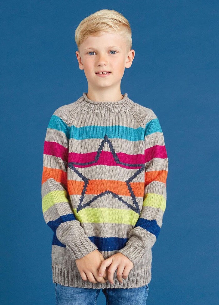 A young child stands against a blue background, wearing a colorful striped sweater with a large star pattern. The sweater has vibrant hues, conveying a cheerful tone.