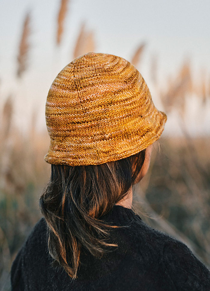Back view of a yellow textured knit hat, the Delmira Hat, worn outdoors with tall grasses in the background.