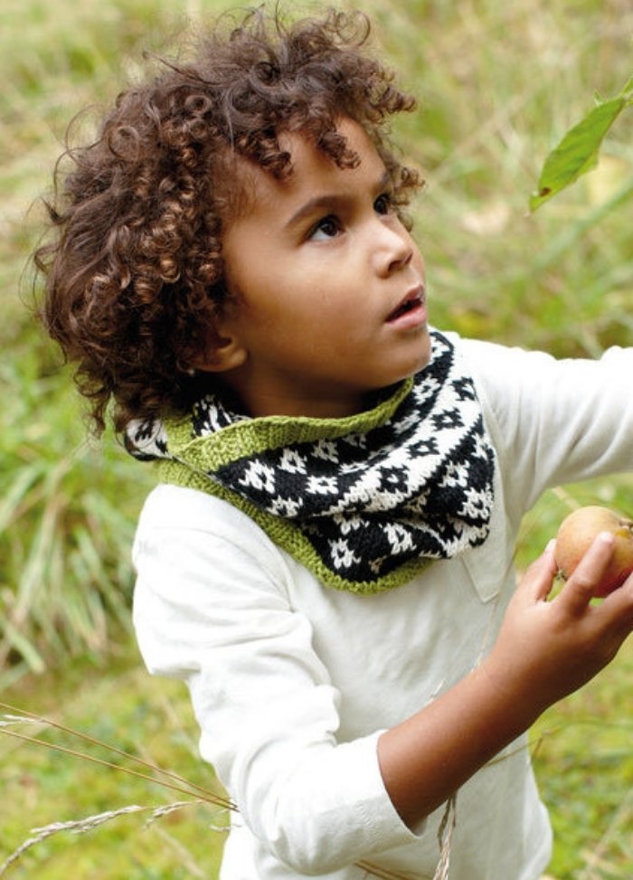 Child in Diamond Sky Cowl with diamond pattern and green edges, outdoors in grassy area.