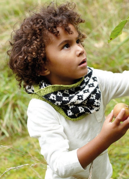 Child in Diamond Sky Cowl with diamond pattern and green edges, outdoors in grassy area.