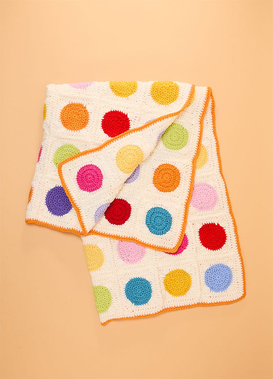 Crocheted Dot Blanket with a white background and evenly spaced colorful circular dots in red, yellow, green, blue, purple, pink, and orange, finished with an orange border – playful and vibrant handmade design.