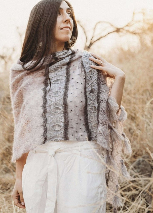 Woman in a knitted shawl poses outdoors in a dry, grassy field. Soft sunlight highlights her serene expression, creating a natural, peaceful mood.