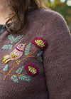Birdie: pink bird perched among red flowers and green leaves embroidered on knit sweater.