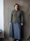 Blomma: yellow floral embroidery arranged as text-like motifs on grey knit cardigan.