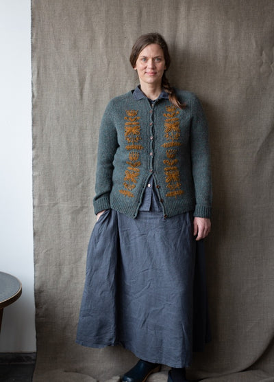 Blomma: yellow floral embroidery arranged as text-like motifs on grey knit cardigan.